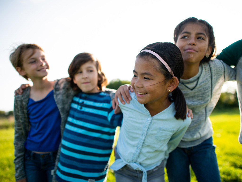 group of diverse children playing outside with arms around each other