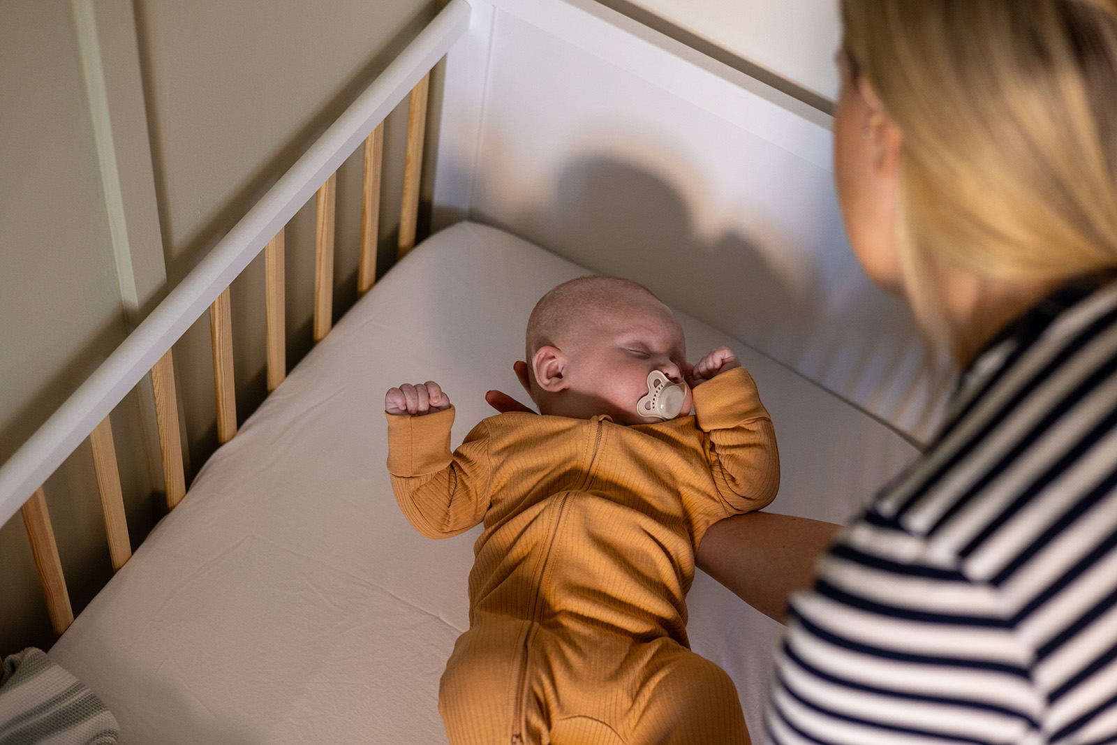 Adult laying sleeping infant down into crib