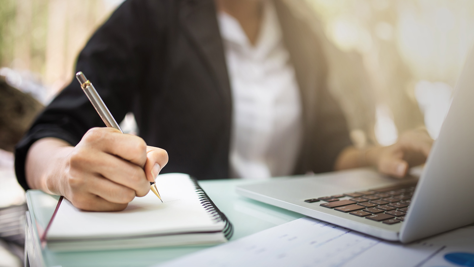Person taking notes while working on laptop